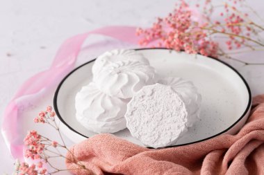 Pembe kurdele ve çiçeklerin yanında beyaz bir arka planda beyaz tabakta beyaz ve pembe marşmelov zephyr. Elma püresi ve yumurta beyazından yapılmış beyaz zefyr. Düşük kalorili tatlılar. Vegan şekerlemesi..