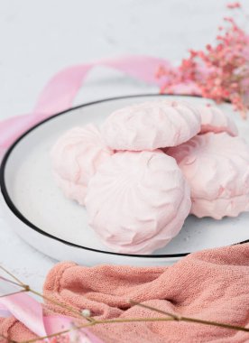 Pembe böğürtlen şekerlemesi beyaz tabakta, arka planda pembe kurdele ve çiçeklerin yanında. Elma sosu ve yumurta beyazından yapılmış beyaz ve pembe zefyr. Düşük kalorili tatlılar. Vegan şekerlemesi..