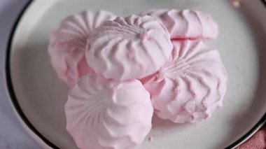 Pembe böğürtlen şekerlemesi beyaz tabakta, arka planda pembe kurdele ve çiçeklerin yanında. Elma sosu ve yumurta beyazından yapılmış beyaz ve pembe zefyr. Düşük kalorili tatlılar. Vegan şekerlemesi..