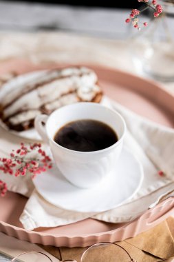 Pembe bir tepsiye konmuş çay tabağında, dumanı tüten kahveyle dolu beyaz bir fincan. Yanında kremalı bir Fransız ekini var. Küçük bir pembe çiçek filizi süsleme katar.