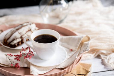 Pembe bir tepsiye konmuş çay tabağında, dumanı tüten kahveyle dolu beyaz bir fincan. Yanında kremalı bir Fransız ekini var. Küçük bir pembe çiçek filizi süsleme katar.