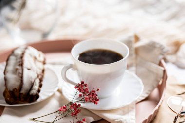 Pembe bir tepsiye konmuş çay tabağında, dumanı tüten kahveyle dolu beyaz bir fincan. Yanında kremalı bir Fransız ekini var. Küçük bir pembe çiçek filizi süsleme katar.