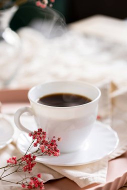 Pembe bir tepsiye konmuş çay tabağında, dumanı tüten kahveyle dolu beyaz bir fincan. Yanında kremalı bir Fransız ekini var. Küçük bir pembe çiçek filizi süsleme katar.