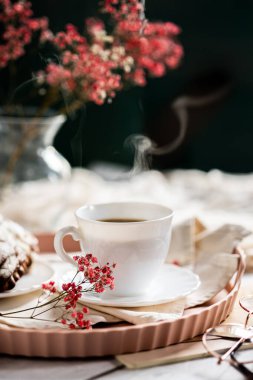 Pembe bir tepsiye konmuş çay tabağında, dumanı tüten kahveyle dolu beyaz bir fincan. Yanında kremalı bir Fransız ekini var. Küçük bir pembe çiçek filizi süsleme katar.