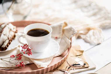 Pembe bir tepsiye konmuş çay tabağında, dumanı tüten kahveyle dolu beyaz bir fincan. Yanında kremalı bir Fransız ekini var. Küçük bir pembe çiçek filizi süsleme katar.