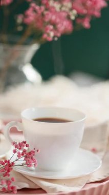 Taze demlenmiş kahve buharları çay tabağında, kremalı, pembe çiçekli, beyaz peçeteli Fransız ekininin yanında. Sabah kahve konsepti. Yüksek kaliteli video