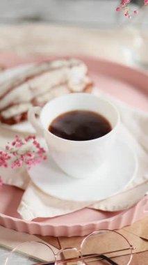 Taze demlenmiş kahve buharları çay tabağında, kremalı, pembe çiçekli, beyaz peçeteli Fransız ekininin yanında. Sabah kahve konsepti. Yüksek kaliteli video