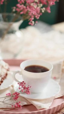 Taze demlenmiş kahve buharları çay tabağında, kremalı, pembe çiçekli, beyaz peçeteli Fransız ekininin yanında. Sabah kahve konsepti. Yüksek kaliteli video