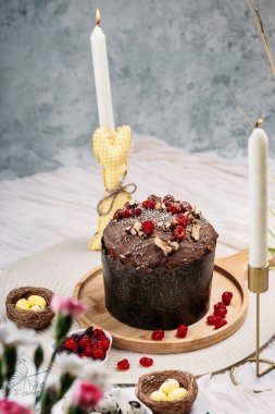 Paskalya pastası, çikolata jöleli paskalya ekmeği kuru kiraz ve cevizle süslenmiş arka planda uzun mumlar, çiçekler, yakınlarda Paskalya tavşanı. Paskalya konsepti