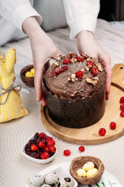 Beyaz gömlekli kadın Paskalya pastası, çikolata kaplı paskalya ekmeği kuru kiraz ve cevizle süslenmiş arka planda uzun mumlar, çiçekler, Paskalya tavşanı. Paskalya konsepti.