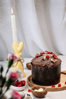 Paskalya pastası, çikolata jöleli paskalya ekmeği kuru kiraz ve cevizle süslenmiş arka planda uzun mumlar, çiçekler, yakınlarda Paskalya tavşanı. Paskalya konsepti
