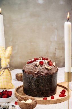 Paskalya pastası, çikolata jöleli paskalya ekmeği kuru kiraz ve cevizle süslenmiş arka planda uzun mumlar, çiçekler, yakınlarda Paskalya tavşanı. Paskalya konsepti