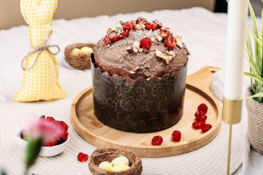 Paskalya pastası, çikolata jöleli paskalya ekmeği kuru kiraz ve cevizle süslenmiş arka planda uzun mumlar, çiçekler, yakınlarda Paskalya tavşanı. Paskalya konsepti