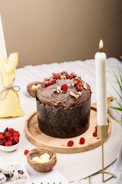 Paskalya pastası, çikolata jöleli paskalya ekmeği kuru kiraz ve cevizle süslenmiş arka planda uzun mumlar, çiçekler, yakınlarda Paskalya tavşanı. Paskalya konsepti