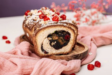 Paskalya ekmeği, haşhaş tohumu dolgulu panettone, fındık, kuru kiraz, açık arkaplanda pembe bir peçetede çikolata jöleli kuru üzüm. Paskalya konsepti