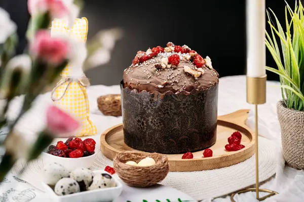 Paskalya pastası, çikolata jöleli paskalya ekmeği kuru kiraz ve cevizle süslenmiş arka planda uzun mumlar, çiçekler, yakınlarda Paskalya tavşanı. Paskalya konsepti