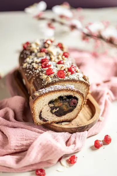 Paskalya ekmeği, haşhaş tohumu dolgulu panettone, fındık, kuru kiraz, açık arkaplanda pembe bir peçetede çikolata jöleli kuru üzüm. Paskalya konsepti