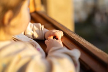 Pencereden dışarı bakan bir çocuğun yakın plan fotoğrafı. Yumuşak güneş ışığı sahneyi aydınlatıyor. Görüntü bir merak ve merak anı yakalar ve onu çocukluk teması için ideal kılar.