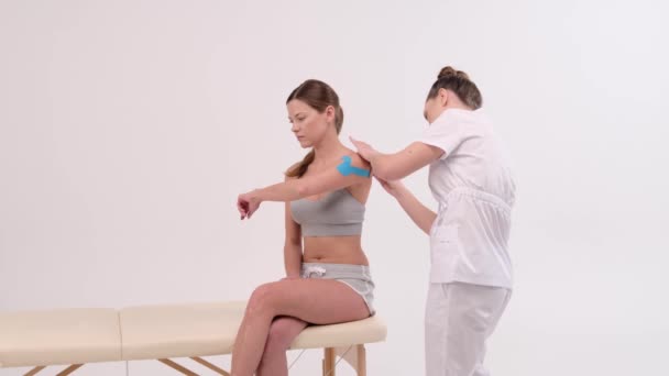 キネシオテープで肩の治療 白い背景に患者の肩の損傷に弾性治療テープを適用する理学療法士 — ストック動画
