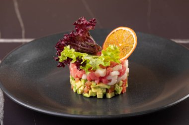 Raw salmon, avocado purple onion salad served in culinary ring on black plate. Black concrete background. restaurant serving