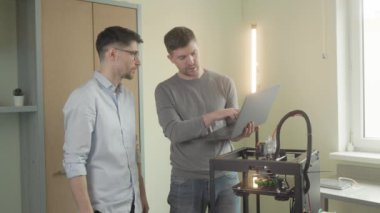 3D yazıcı. Katkı maddesi üretimi. İki erkek mühendis projeyi tartışıyor 3D yazıcı makinesinin yeni bileşenleri modellemesini izliyorlar. Adamlar dizüstü bilgisayar kullanıyor.