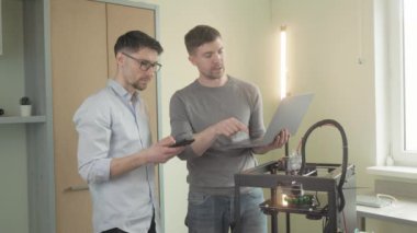 3D yazıcı. Katkı maddesi üretimi. İki erkek çalışan arkadaş gelecekteki projeyi tartışıyor 3D yazıcı makinesinin yeni bileşenleri modellemesini izliyorlar. Modern tasarım teknolojisi kavramı