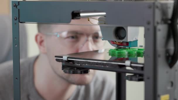 3Dプリンタで緑のプラスチックから歯車の詳細を印刷するプロセスを見てメガネをかけているエンジニアの男 現代のデザイン技術の概念は — ストック動画