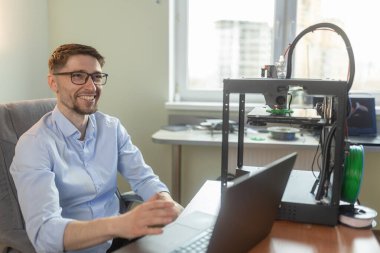 Laboratuvarda dizüstü bilgisayarla çalışan Mühendislik öğrencisinin gülümseyen portresi, arka planda 3D yazıcı. Modern tasarım teknolojisi kavramı