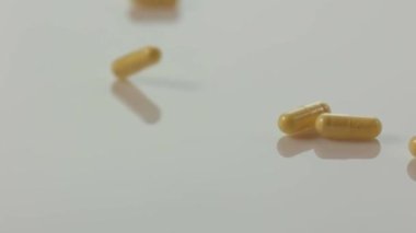 Sarı ilaç hapları bembeyaz saf yüzeye yavaş çekimde düşüyor. B vitamini kompleksi