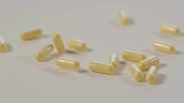 Sarı ilaç hapları bembeyaz saf yüzeye yavaş çekimde düşüyor. B vitamini kompleksi
