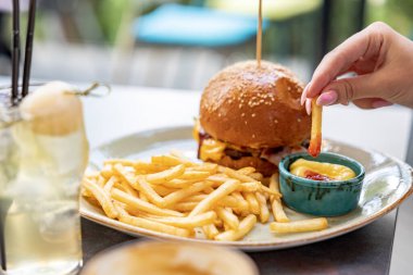 Burger Fotoğrafı. Restoran ve kafede yemek fotoğrafçısı burger ve patates kızartması. Patatesleri sosa batırır.