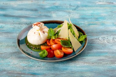 Mozzarella soslu domates salatası, fesleğen sosu, zeytinyağı, sarımsak, parmesan ve fesleğenden yapılan pesto, mavi arkaplanda. Orijinal restoran poşette mozzarella servis ediyor.