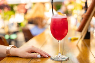 Restoranda bir kadının elinin yanındaki masada kırmızı bir kokteyl duruyor. Yaz tazeleyici kokteyl.