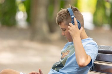 Dışarıda kulaklıkları olan, gülen 10 yaşında bir çocuk. Çocukluk. Öğrenci çocuk. yaz.