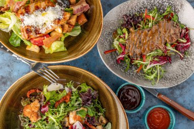 Üç tabak salatanın üst görüntüsü. Dilimlenmiş biftekli yeşil yapraklı biftek salata tavuk göğsü, roka ve mavi salata ile taze salata gri taşlı sezar salata.