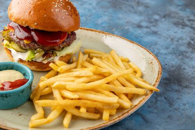 Marullu sığır burger, patates kızartması ve soslu turşu ve gri-mavi arka planda. Restoran servisi.