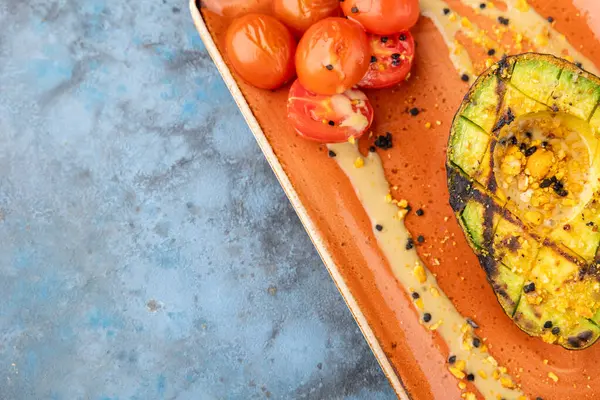 Grilled avocado with cherry tomatoes and cheese sauce on plate. Top view, copy space