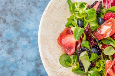 Jambonlu ve dutlu lezzetli salata. Tabakta yaz salatası. Mavi arkaplan