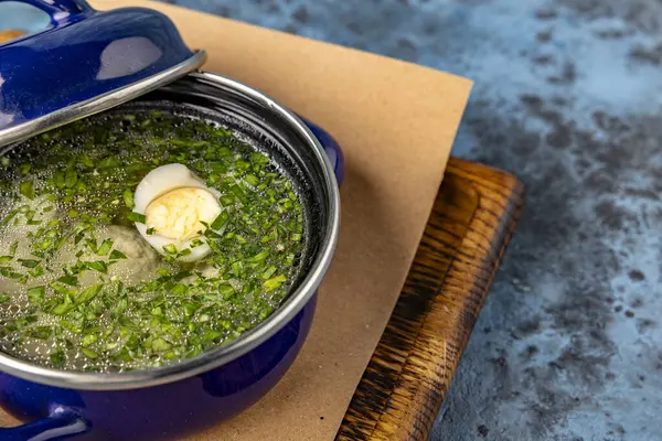 stock image broth with greens, boiled egg in a saucepan on a wooden board. Restaurant service. View from above. Place for text. Childrens menu