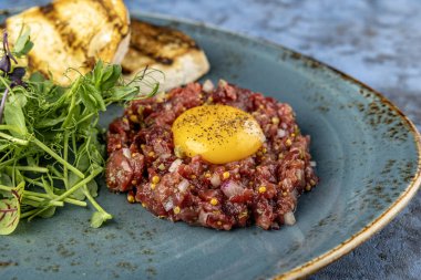 Dana etli tartar, bıldırcın yumurtası ve kızarmış ekmek. Mikroyeşilliklerle servis edilen restoran. mavi arkaplan