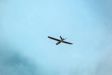 Bir dron, ön planda bulanık yeşil yapraklarla çevrili, dağınık bulutlu, parlak mavi bir gökyüzüne karşı uçar. Hava keşifleri için. Ukrayna yapımı İHA