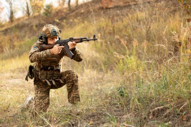 Askeri üniformalı Ukrayna askeri, saldırı tüfeği ve Ukrayna bayrağı taşıyan asker. AK tüfekli Ukraynalı asker. Savaş meydanında makineli tüfekli bir asker