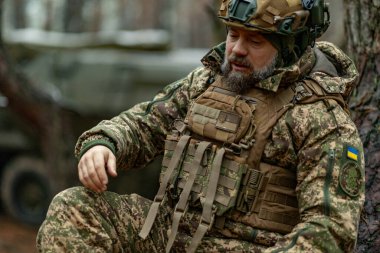 Yorgun Ukraynalı asker bir savaştan ya da savaş görevinden sonra dinlenmek için bir ağacın yanına oturur.