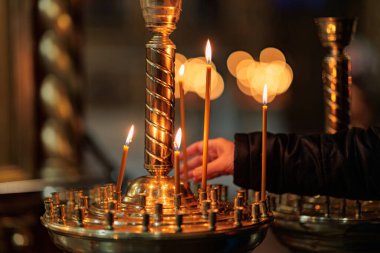 Kilisede mum yakan bir adam. Tapınakta mum yakmak, arka planda haçla yanan mumlar, Hıristiyan dini kavramı, kurtuluşun duaları.