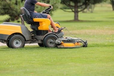 Golf sahasının çimlerinde çim biçme makinesi süren bir adam.