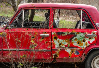 Ukrayna 'da savaş. 2022 Rus istilası Ukrayna. Kırsal kesimde. Yıkılmış bir sivil araba yolun kenarında duruyor. Arabanın gövdesinde kurşun delikleri ve kıymıklar var.