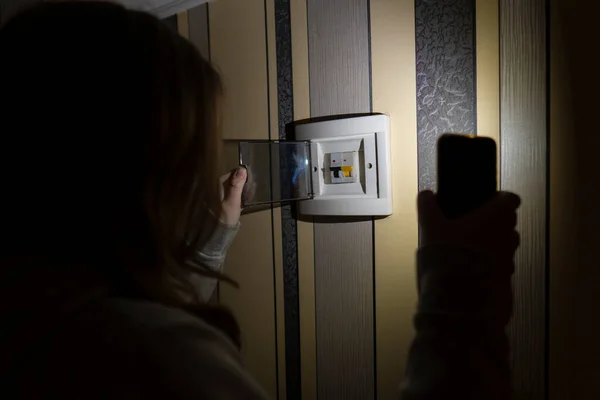 stock image Blackout. Energy crisis. Destruction of infrastructure. Power outage concept. A girl with a smartphone in her hands checks the electrical switchboard in the room