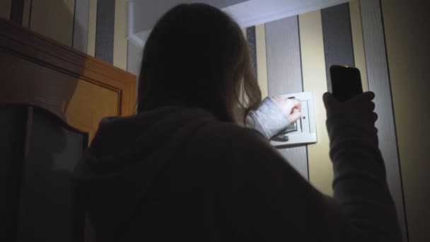 停電だ エネルギー危機 インフラの破壊 停電の概念 スマートフォンを手にした少女が部屋の電気パネルをチェックする 固定カメラ — ストック動画
