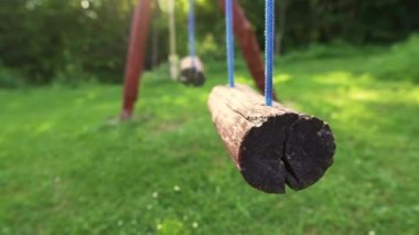 Yaz. Güneşli bir gün. Boş eski ahşap salıncaklar yeşil çimlerde sallanıyor. Yakın plan. Sabit Kamera