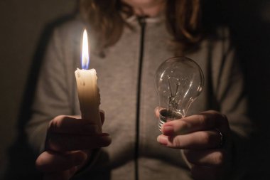 Kesinti. Altyapı tahribatı. Enerji krizi. Elektrik kesintisi konsepti. Kız elinde bir ampul ve yanan bir mum tutuyor. Yakın plan.
